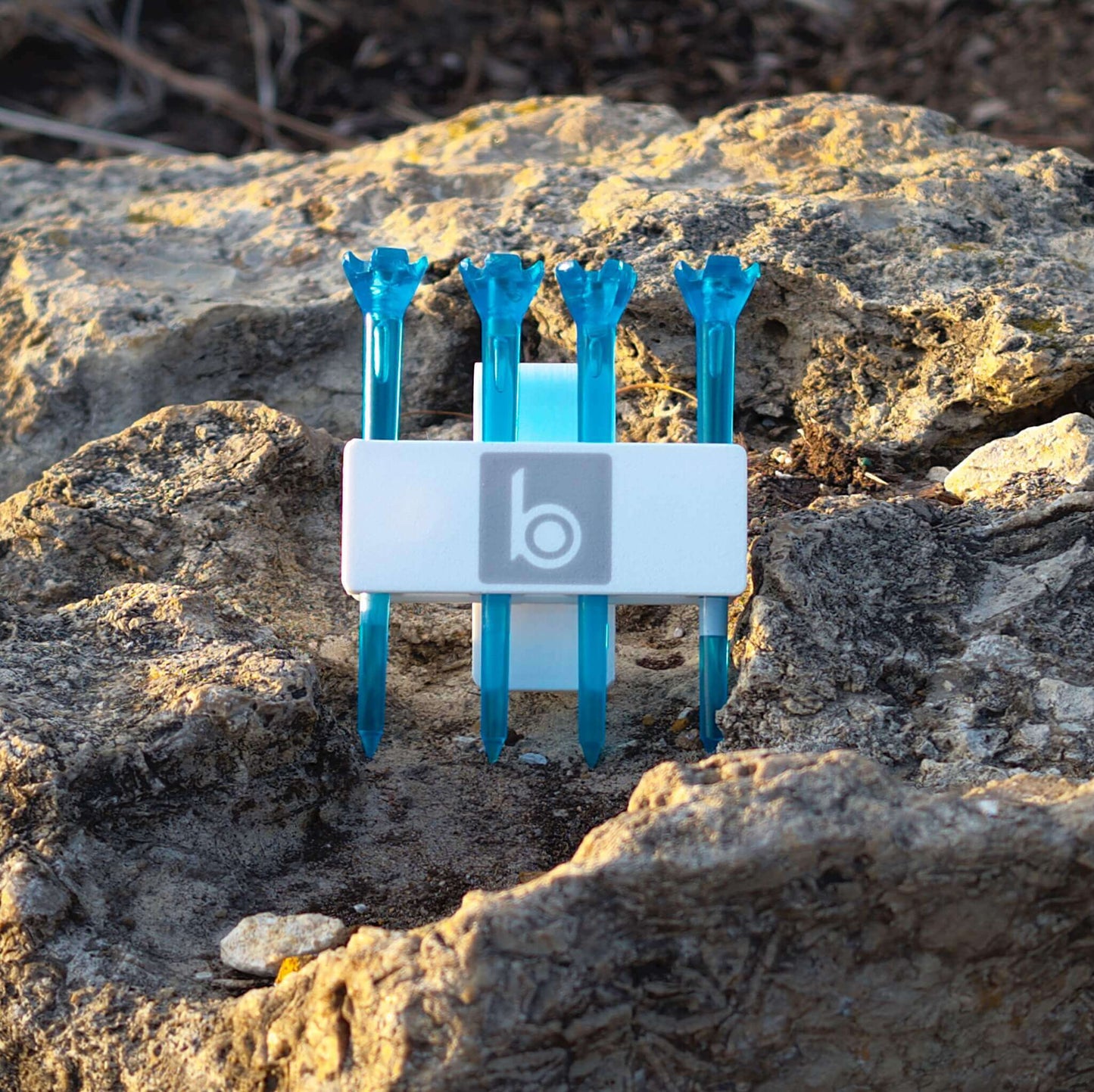 ProtoClip MINI 2 in white with four blue golf tees on a rocky surface, designed for easy access on the golf course.